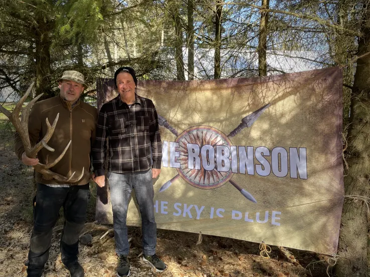 To voksne mænd foran et flag med teksten Robinson og The Sky Is Blue.